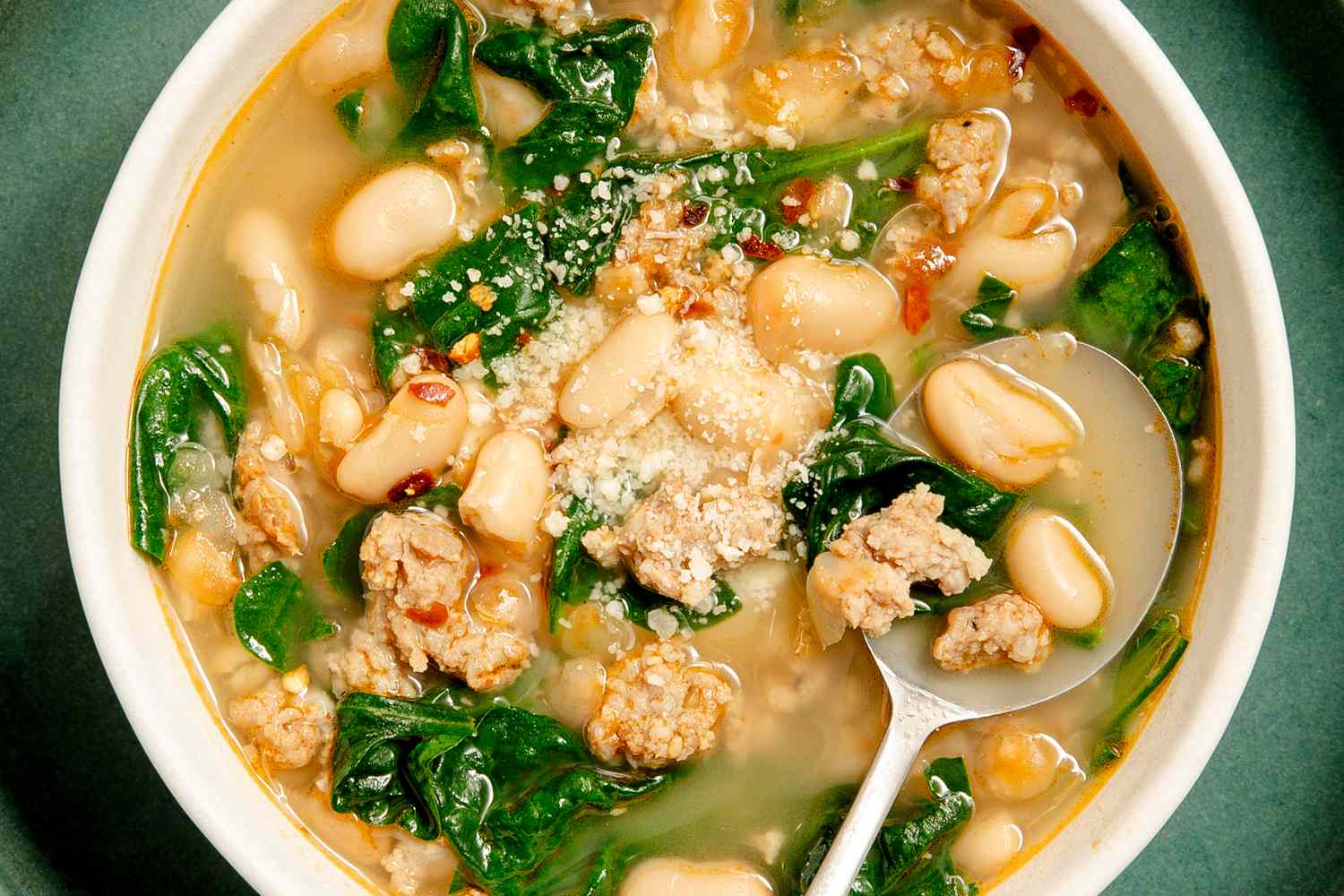 A white bowl with a soup filled with kale, white bean and sausage