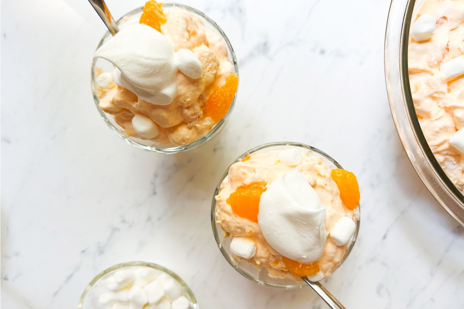 Orange creamsicle salad served in small glass bowls topped with whipped cream and marshmallows