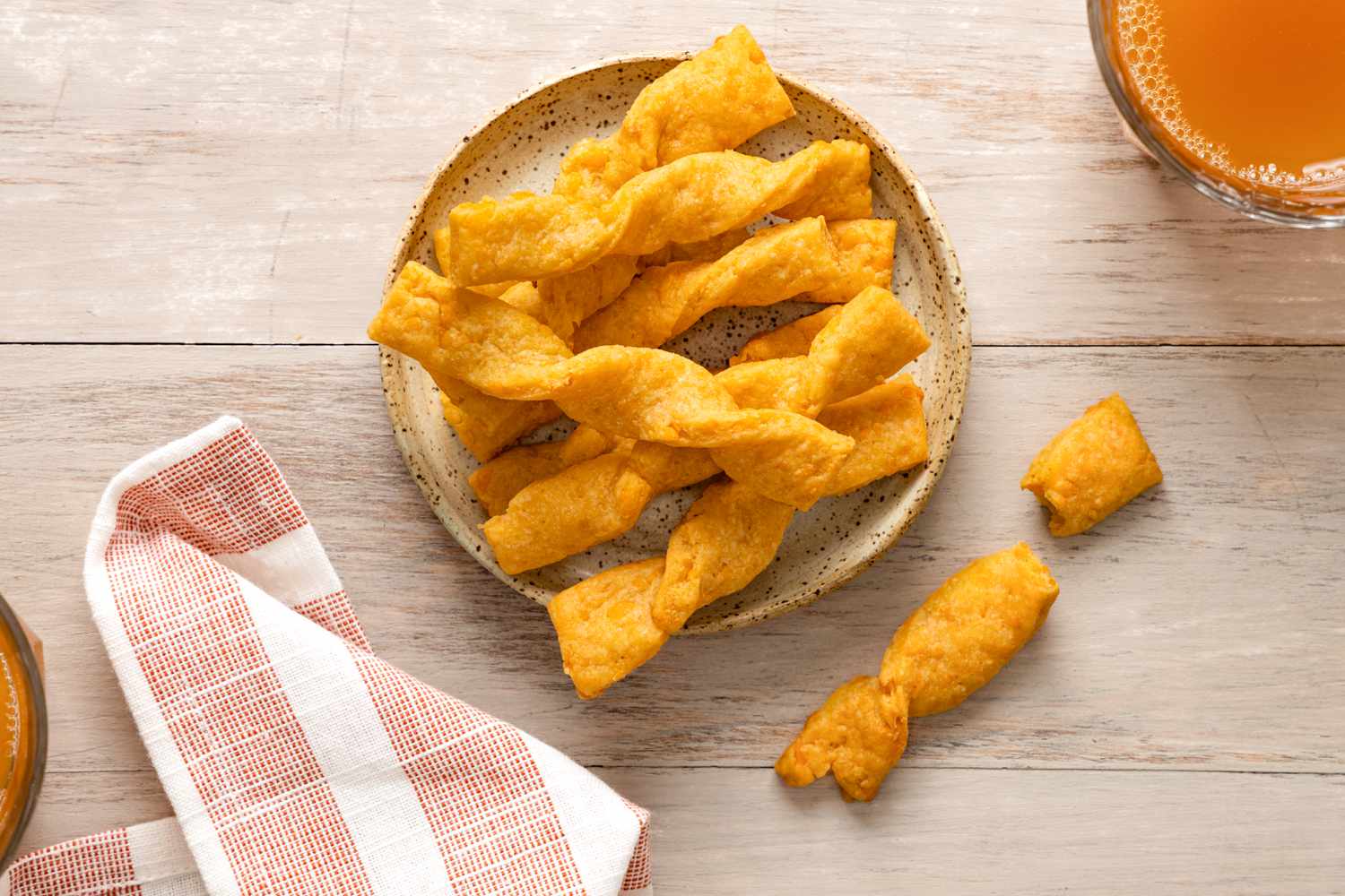 Twisted Cheese Straws on a Plate Next to a Drink and a Kitchen Towel.