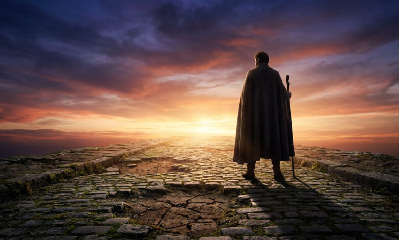 Un voyageur en cape se tient sur un chemin pavé ancien face à un coucher de soleil dramatique.